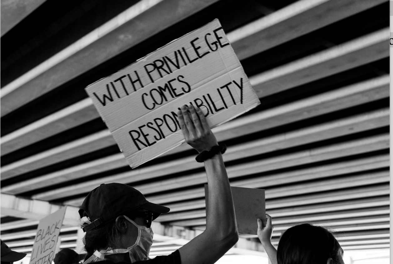 A person in a protest, holding a sign that reads "With privilege comes responsibility."